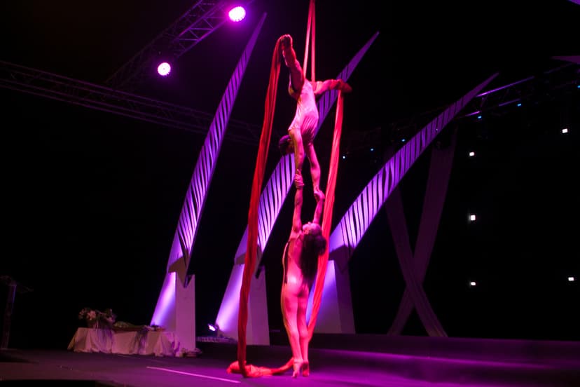 Acróbatas en telas aéreas rojas con iluminación escénica magenta y arquitectura escenográfica