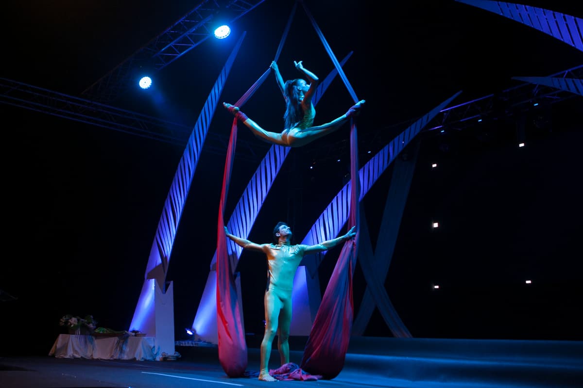 Performer de telas aéreas con los brazos extendidos sobre un escenario con luz azul
