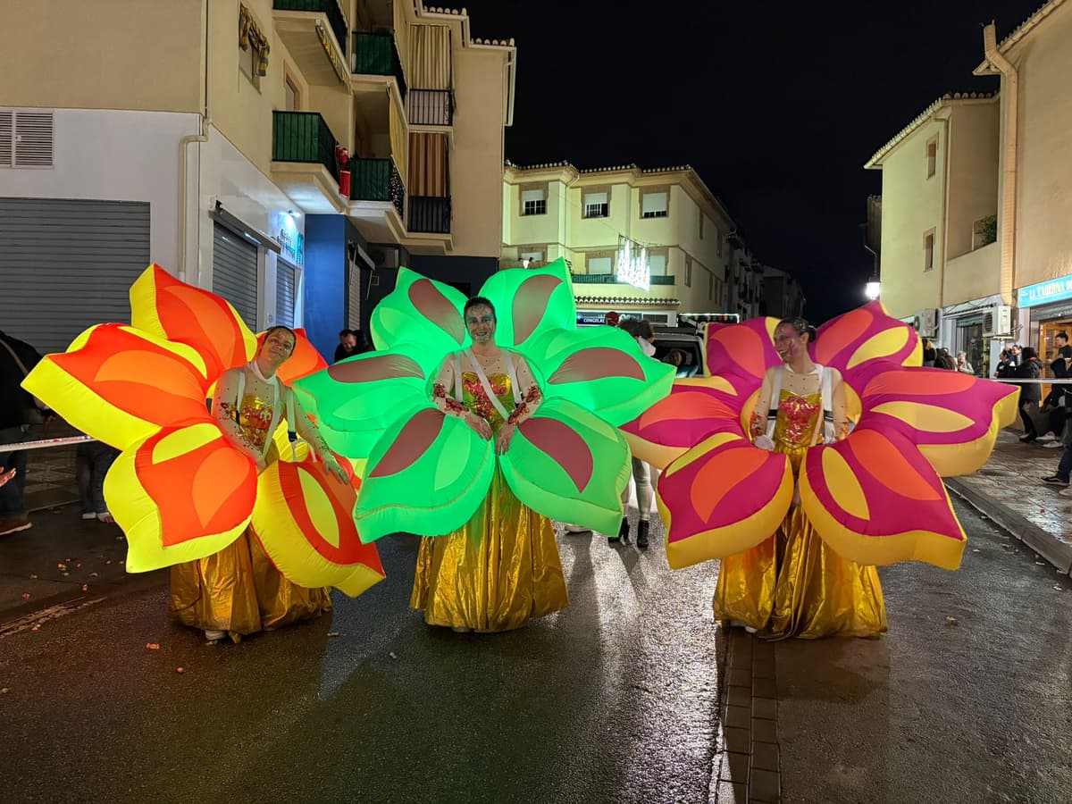 Tres animadores dentro de trajes hinchables de flores naranja, verde y rosa en una calle