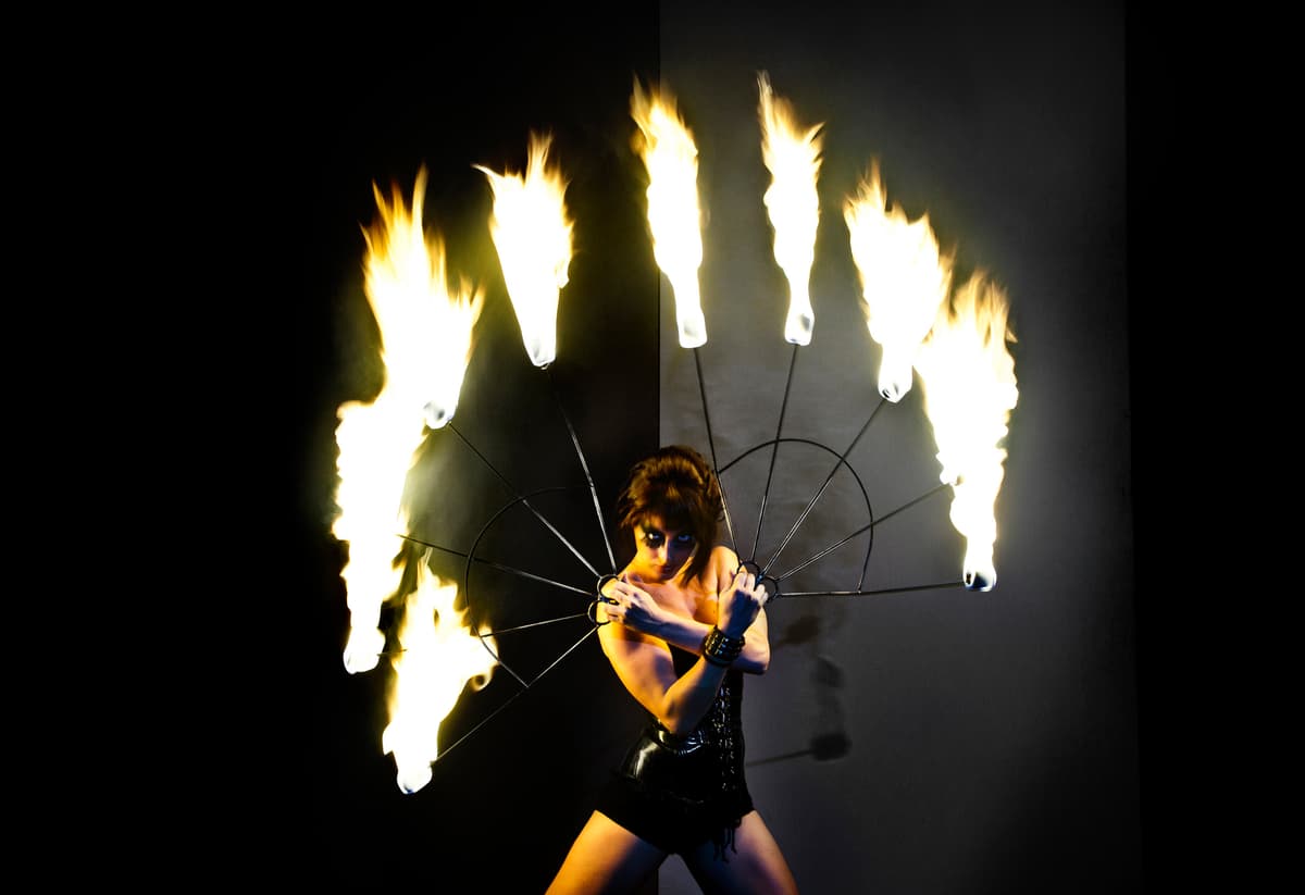 Artista de fuego girando abanicos encendidos sobre fondo oscuro en un montaje escénico