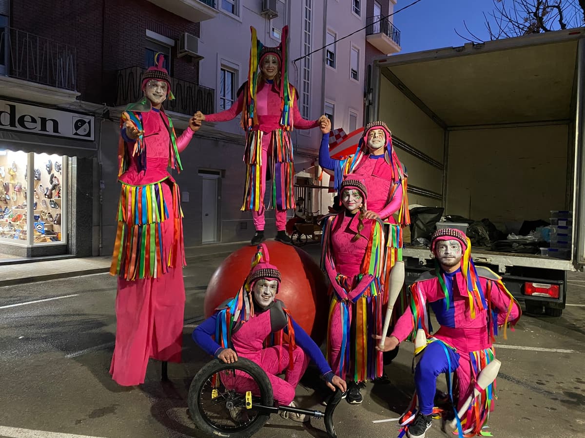 Grupo de zancudos circenses avanzando por una calle en un pasacalles diurno