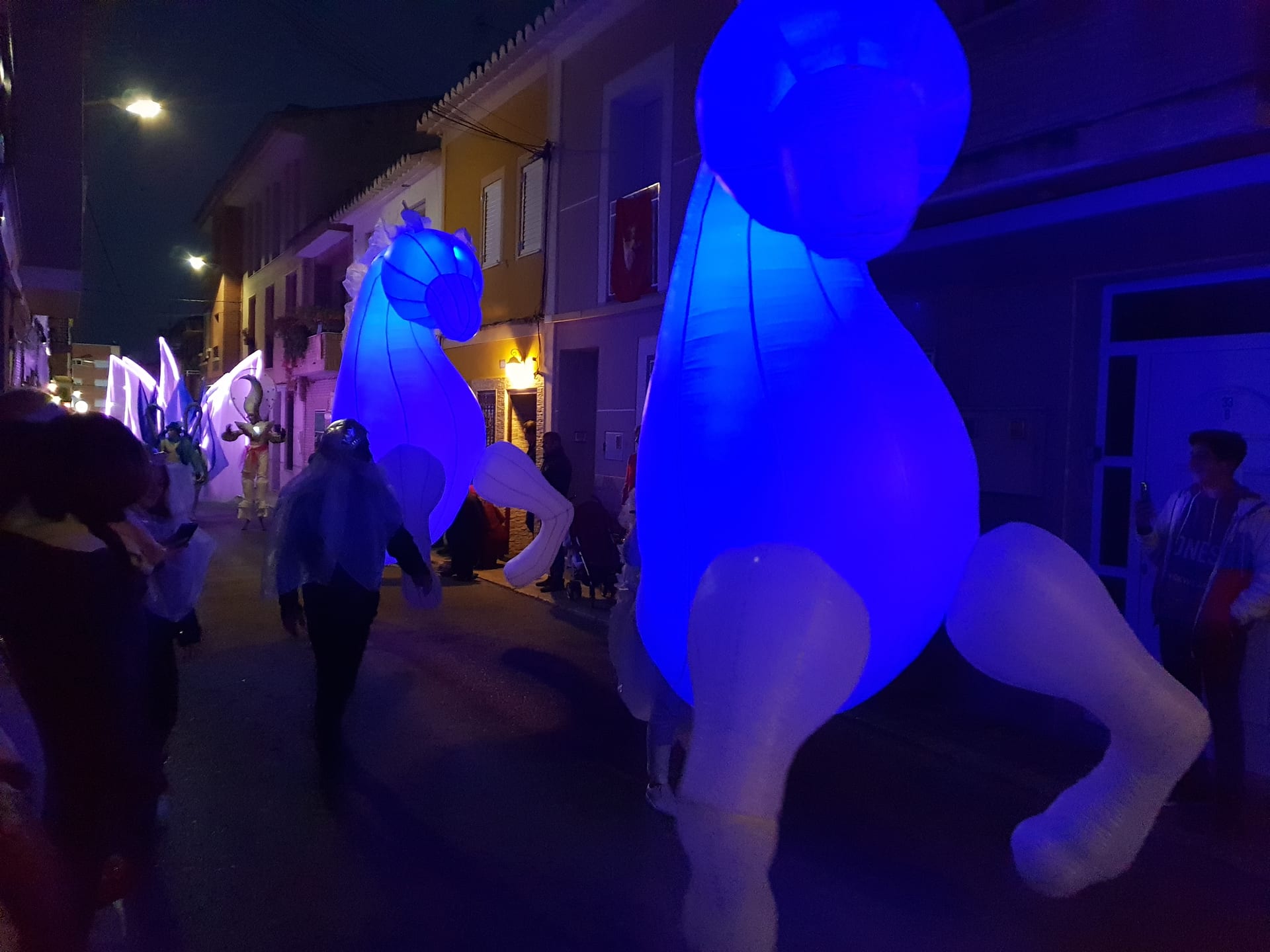 Caballos hinchables iluminados en azul en cabalgata de Reyes nocturna por calle estrecha