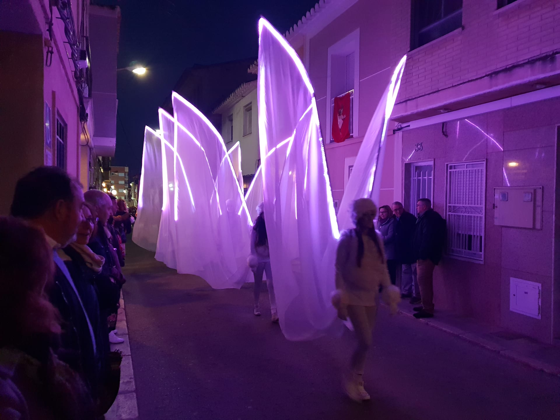Velos LED gigantes iluminados en magenta sobre calle estrecha en pasacalles nocturno